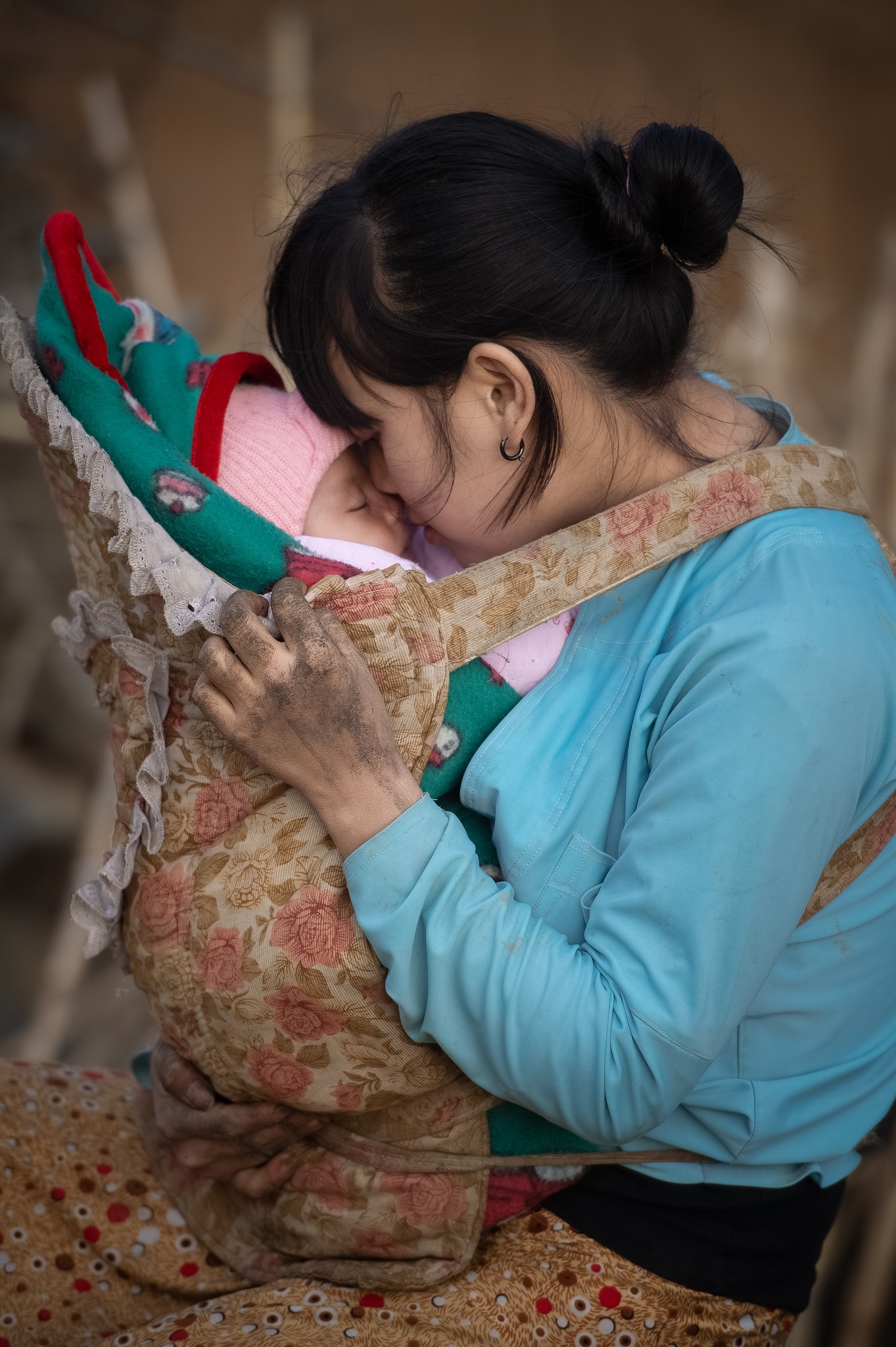 Người mẹ trẻ hôn đứa con địu trên lưng