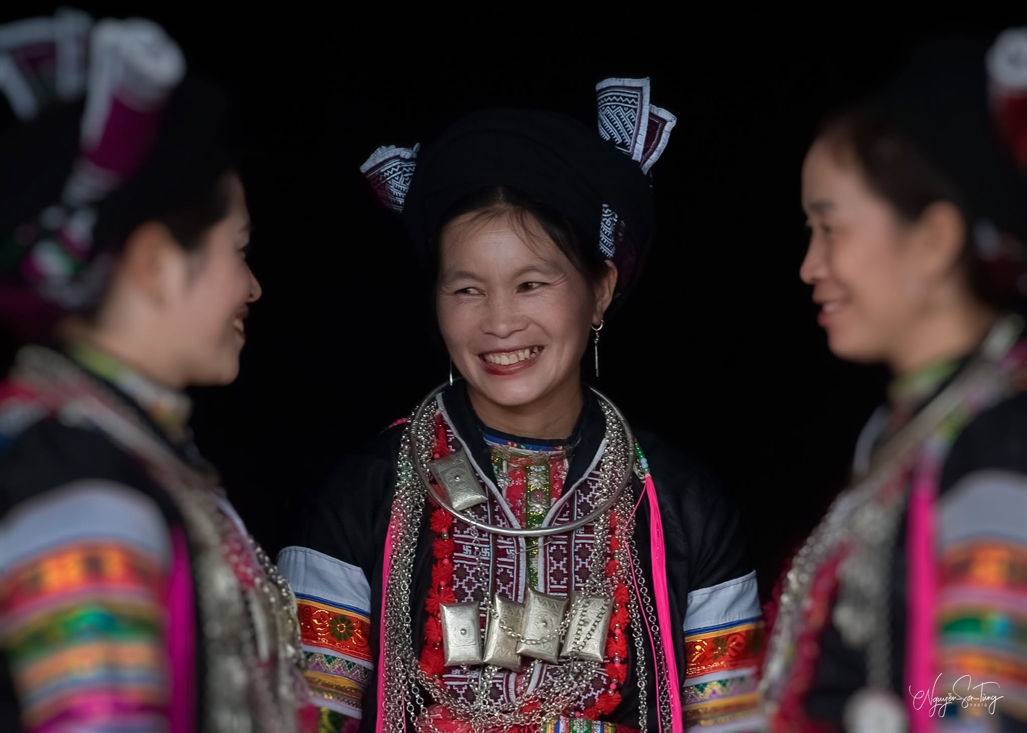 Ba phụ nữ Dao đỏ cười rạng rỡ, người ở giữa đeo nhiều bạc