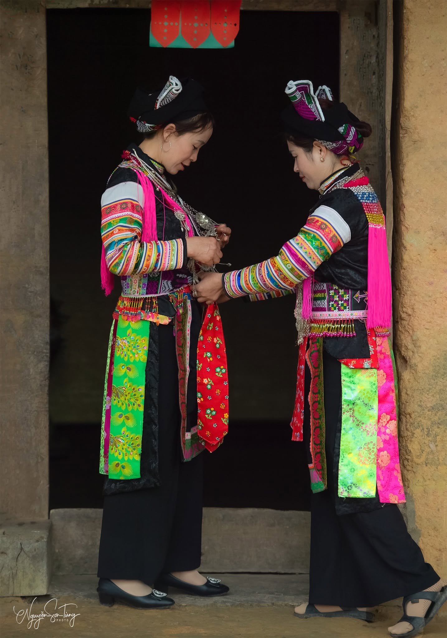 Hai phụ nữ Dao đỏ chỉnh áo cho nhau bên cửa