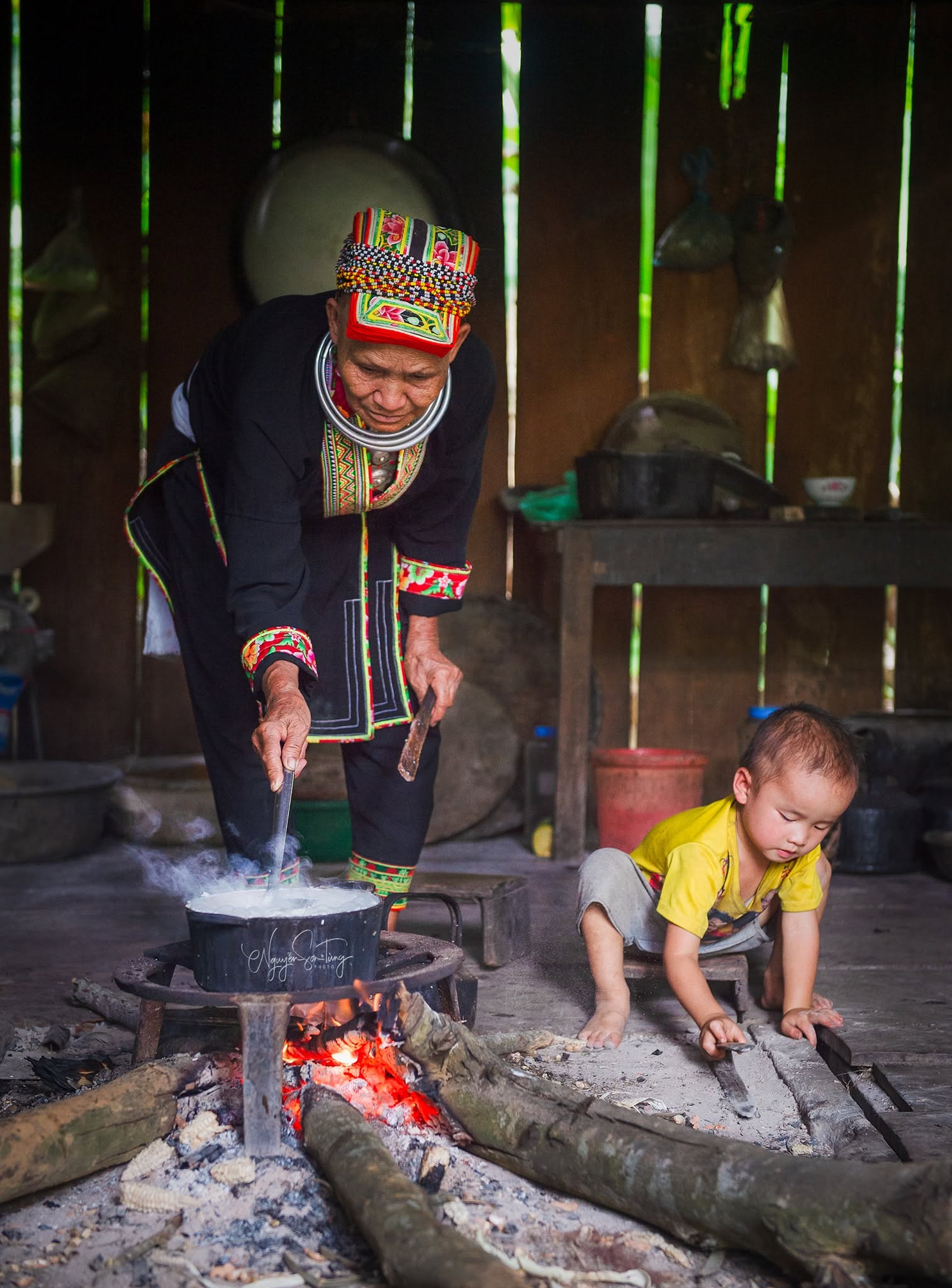 Cụ bà Dao khuấy nồi trên bếp lửa, cháu nhỏ ngồi chơi bên cạnh