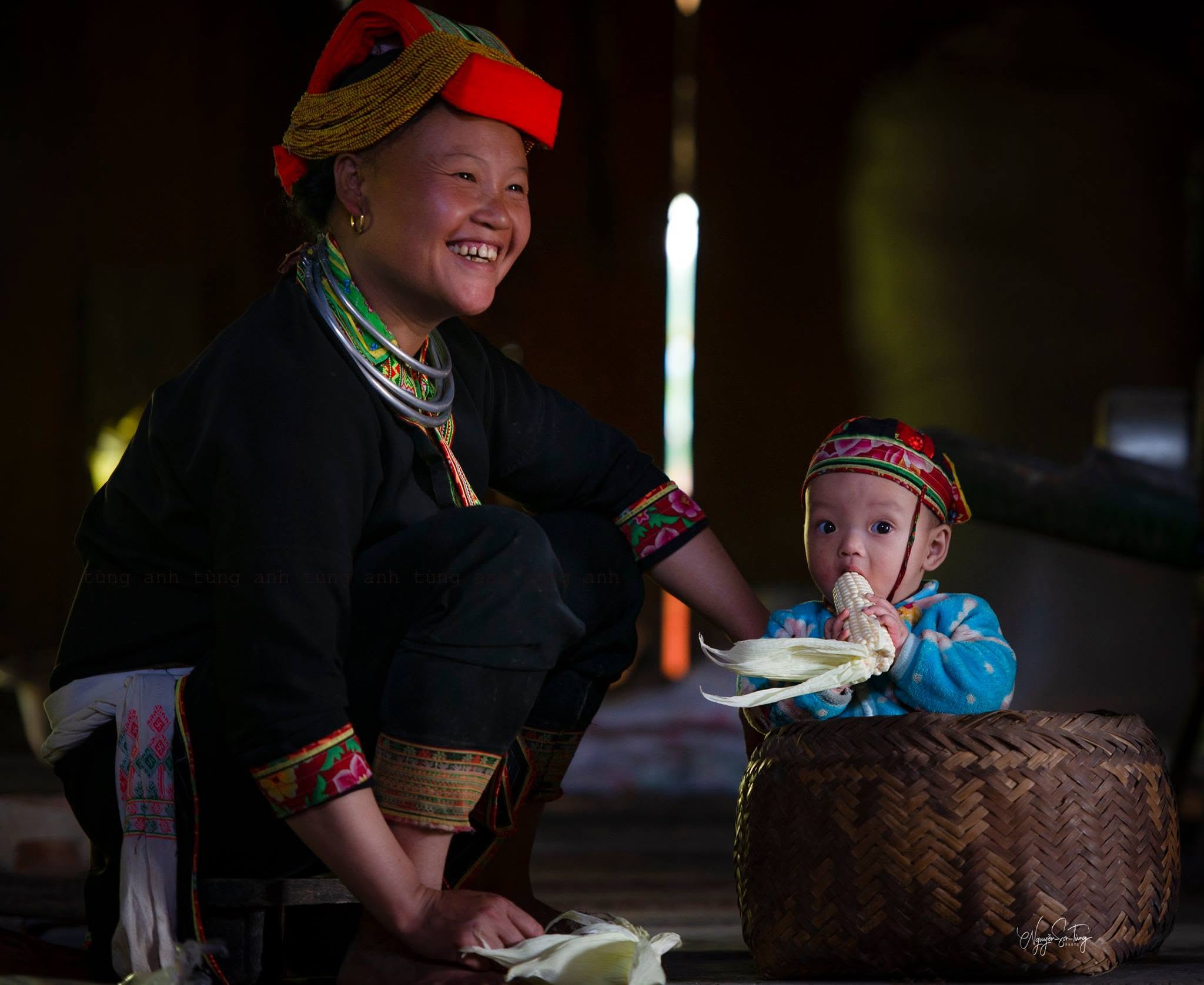 Em bé Dao ôm bắp ngô ngồi bên hiên nhà